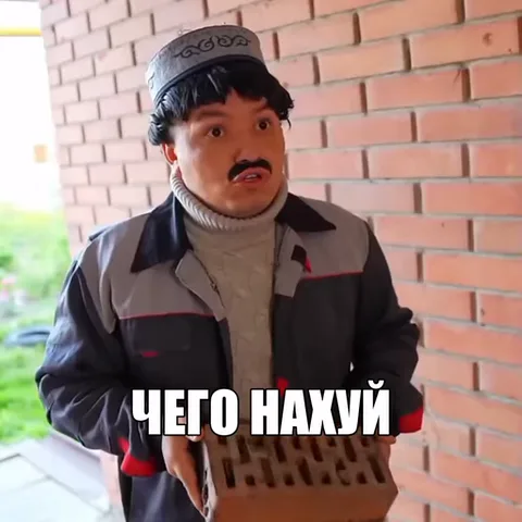 Мужчина с усами в тюбетейке и серой куртке разводит руками на фоне кирпичной стены, надпись «чего нахуй».