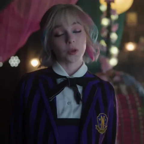 Анимация Энид Синклер из сериала «Уэнсдей», которая закатывает глаза на фоне вечеринки.