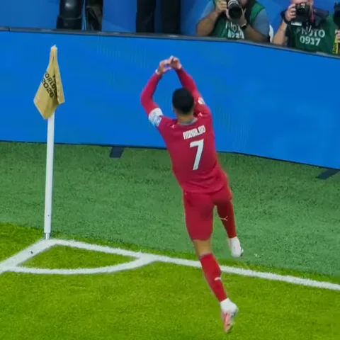 Игрок в красной футболке с номером 7 на спине подпрыгивает на поле перед рекламными щитами.