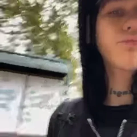 Видео с человеком в темной одежде, который поднимает руку на фоне деревьев.