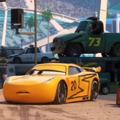 Анимация с жёлтым гоночным автомобилем Круз Рамирес номер 20, который стоит на фоне стадиона и эвакуатора.