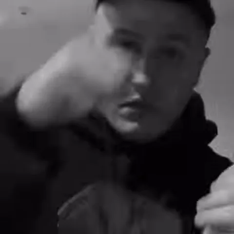 Мужчина в кепке на черно-белом видео размышляет, поднеся руку к лицу.