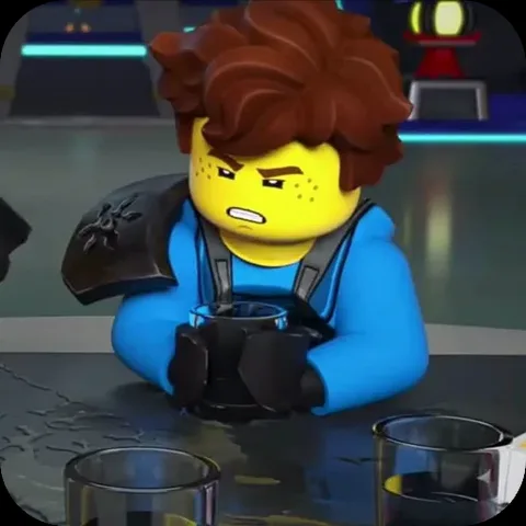 Анимация персонажа Джея из LEGO Ninjago в синем костюме, который сидит за столом и держит кружку с раздраженным выражением лица.