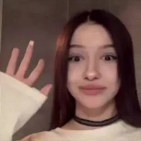 Девушка с длинными темными волосами машет рукой перед камерой.