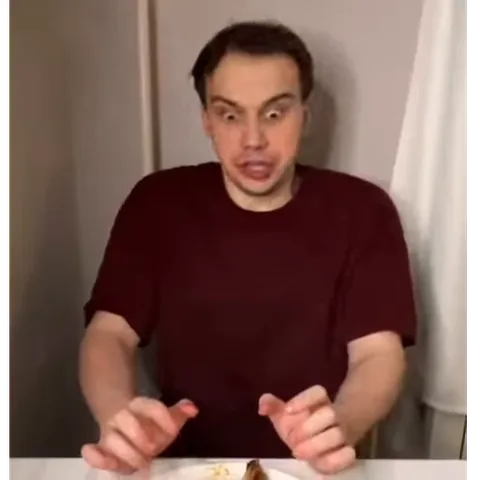 Человек в бордовой футболке с выпученными глазами и трясущимися руками реагирует на еду перед ним.
