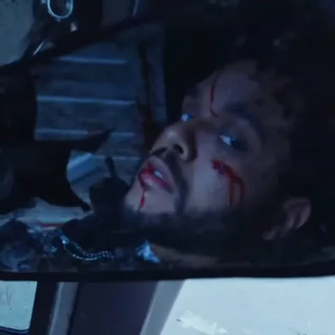 Отражение лица The Weeknd с кровоподтёками в зеркале заднего вида автомобиля