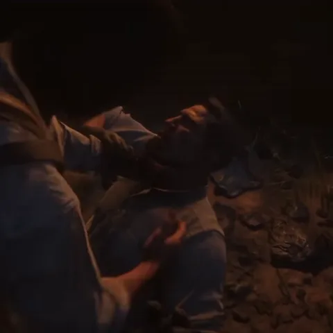Анимация из игры Red Dead Redemption 2: один персонаж в белой рубашке душит другого, лежащего на земле в темноте.