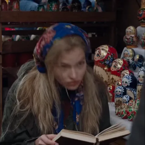 Девушка в платке держит открытую книгу, смотрит в сторону и машет рукой.