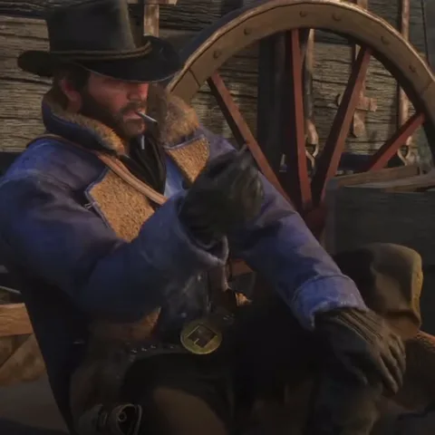 Анимация из игры Red Dead Redemption 2: персонаж Артур Морган в шляпе и тёплой куртке закуривает, сидя рядом с колесом телеги.