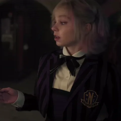 Анимация Энид Синклер из сериала «Уэнсдей», которая размахивает рукой во время разговора и смотрит в сторону.