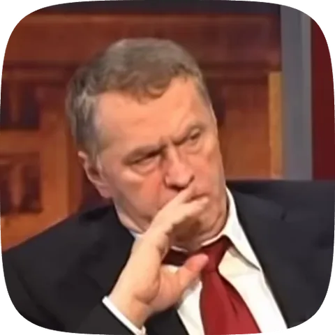 Политик Владимир Жириновский в костюме и красном галстуке держит руку у рта, глядя в сторону.