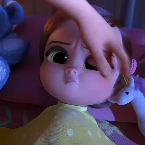 3D-персонаж младенца с большими зелеными глазами и нахмуренными бровями лежит под одеялом, рядом игрушка единорог.