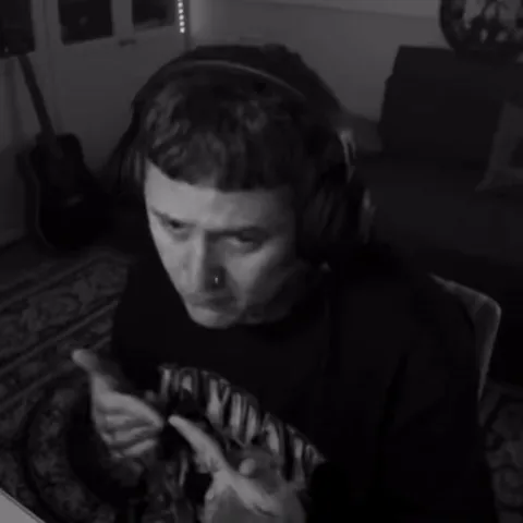 Чёрно-белое видео, где молодой человек в наушниках прикрывает рот рукой и смотрит на зрителя с выражением смущения.