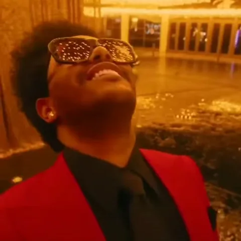 Анимация The Weeknd, который смеется, запрокинув голову, в красном костюме и светящихся очках.
