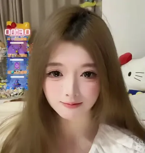 Светловолосая девушка улыбается в камеру, позади нее сидит игрушка Hello Kitty.