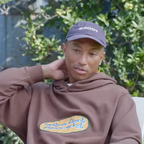 Анимация Pharrell Williams в кепке BADOT и худи, который держит руку у лица.