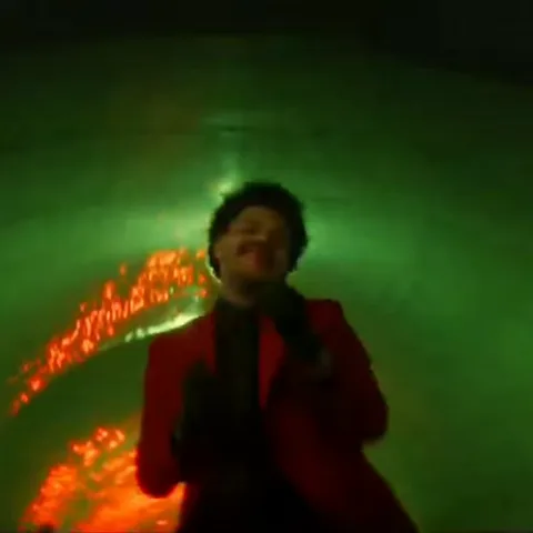 Анимация с певцом The Weeknd в красном пиджаке, который танцует на фоне огня и зеленого света.