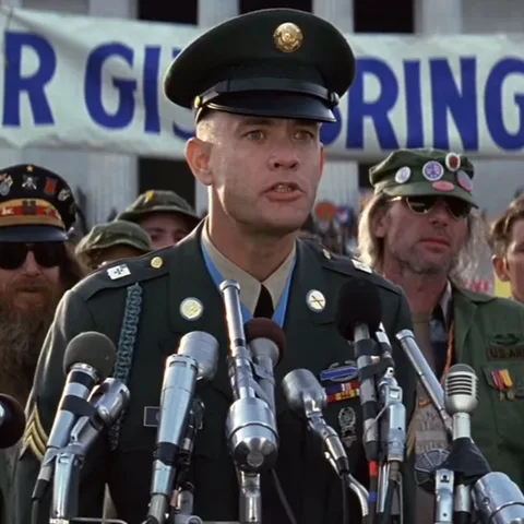 Том Хэнкс в военной форме выступает с речью на фоне плаката "Forrest Gump".