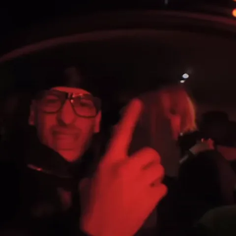Два парня в темноте в машине показывают средний палец, затем крупный план красного логотипа.