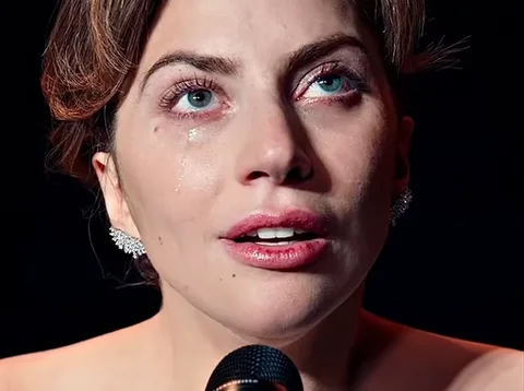 Lady Gaga с закрытыми глазами и слезами на лице держит микрофон перед собой.