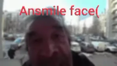 Крупный план лица пожилого мужчины, который кричит в камеру на фоне улицы с машинами.
