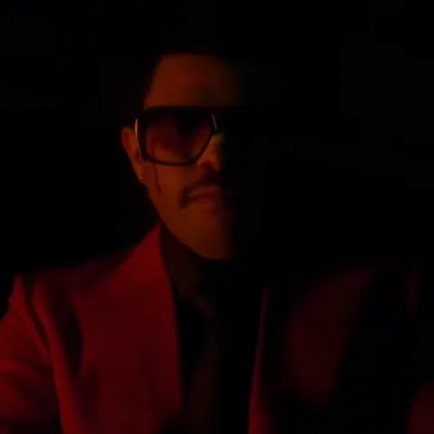 Анимация The Weeknd в красном костюме и темных очках, который наклоняет голову назад под зеленым светом.
