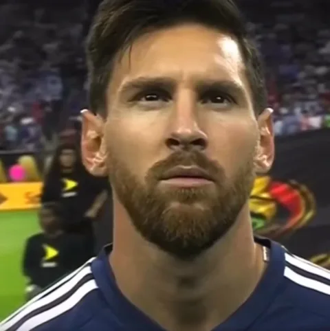 Крупный план Лионеля Месси в синей форме с белыми полосами Adidas, который смотрит прямо перед собой во время футбольного матча.