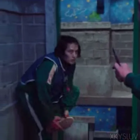 Молодой человек в спортивном костюме игры в кальмара держит перед собой подошву от кроссовка, защищаясь от направленного на него клинка.