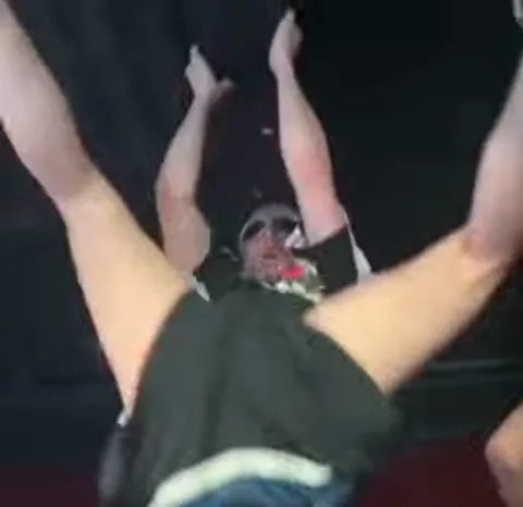 Tommy Cash на концерте поднимает руки и разводит ноги в стороны, демонстрируя дерзкое поведение.