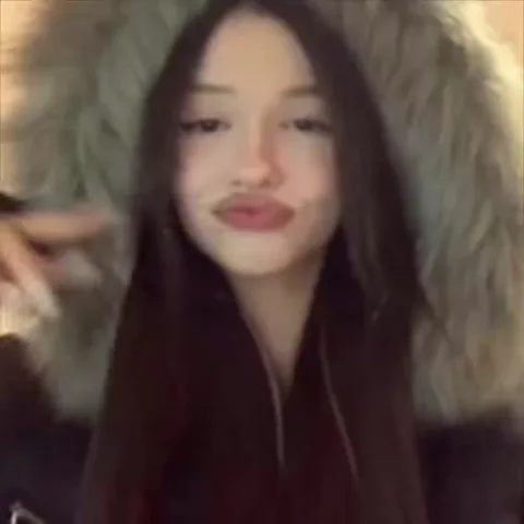 Крупный план девушки в меховом капюшоне, которая смешно морщится и высовывает язык.
