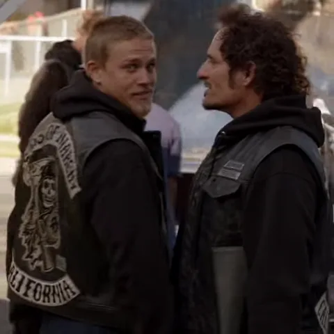 Двое мужчин в черных кожаных жилетах с нашивками Sons of Anarchy California улыбаются друг другу во время разговора.