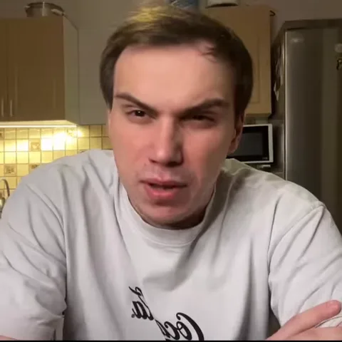 Парень в белой футболке на кухне показывает кулак прямо в объектив камеры.
