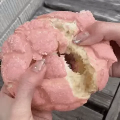 Крупный план рук, которые разрывают большую мягкую булочку с розовой корочкой и светлым мякишем.
