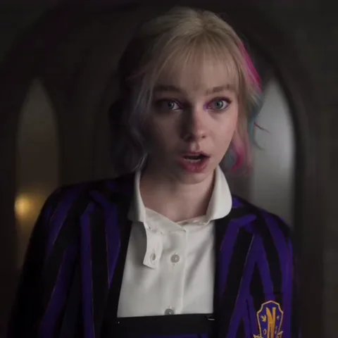 Анимация показывает Энид Синклер из сериала «Уэнсдей», которая сначала удивлённо смотрит прямо перед собой, открыв рот, а затем поворачивается спиной к камере и идёт прочь. На заднем плане видно цветное витражное окно.