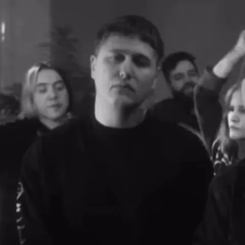 Чёрно-белая анимация: парень в тёмной одежде сохраняет полное безразличие, игнорируя шумную компанию позади себя.