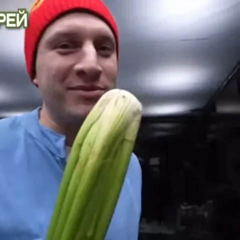 Человек в шапке ест сырой сельдерей крупным планом.