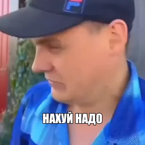 Бритоголовый мужчина в синем костюме и черной кепке, с нарисованным синяком под левым глазом, кричит надпись «НАХУЙ НАДО».