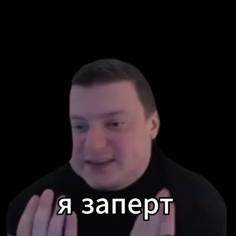 Крупный план мужчины с короткими волосами и бородой, который разговаривает и показывает жесты руками на фоне черного цвета. Внизу идут субтитры с фразой про остров и Интерпол.