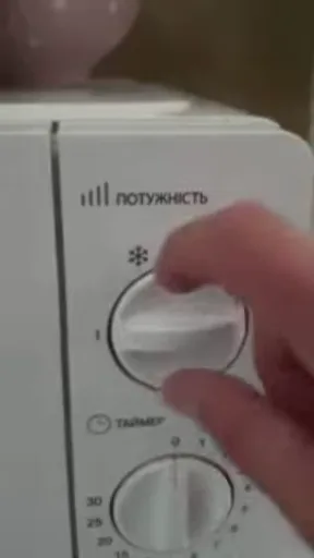 Крупный план руки, которая крутит белую ручку переключателя мощности на панели бытового прибора.