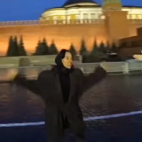 Анимация с девушкой в черном пальто, которая танцует на улице у подсвеченной кирпичной стены.
