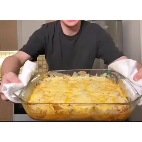 Молодой человек улыбается и демонстрирует готовую запеканку в форме.