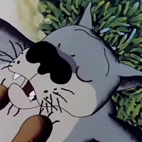 Крупный план серого кота с жёлтыми глазами, лежащего на зелёной траве. Кот часто моргает, его пасть слегка приоткрыта.