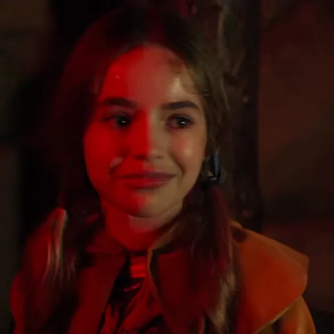 Крупный план лица девочки Холли Уилер из сериала «Очень странные дела», которая улыбается под красным освещением.