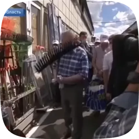 Анимация показывает, как мужчина в клетчатой рубашке на улице берет веерные грабли с витрины магазина.