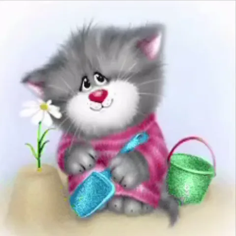 Серый пушистый котёнок в розовом свитере играет с игрушечной лопаткой в песочнице рядом с ромашкой и зелёным ведёрком.