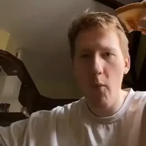 Молодой человек поднимает кружку к лицу и пьет из нее.