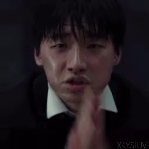 Крупный план мужчины в темном костюме, который прижимает ладони друг к другу перед лицом в жесте мольбы, его глаза полны ужаса.