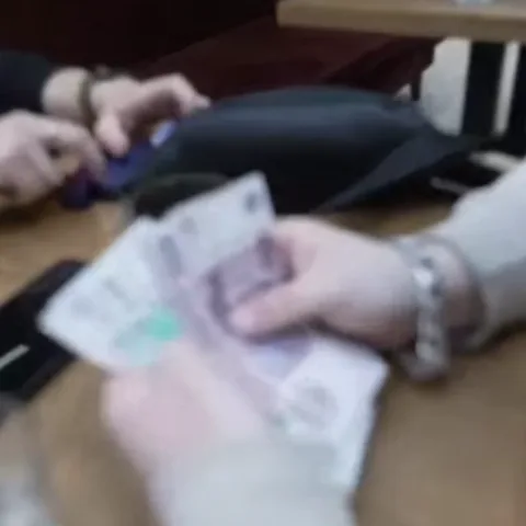 Мужские руки в светлом свитере перебирают стопку российских рублей на деревянном столе.