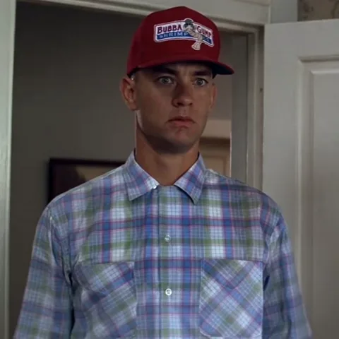 Мужчина в красной кепке с надписью Bubba Gump Shrimp Co. и клетчатой рубашке смотрит прямо перед собой, затем медленно поворачивает голову.