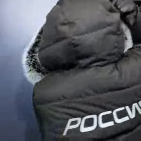 Мужчина в зимней куртке с надписью Россия на спине поворачивается и демонстрирует веер из денежных купюр.